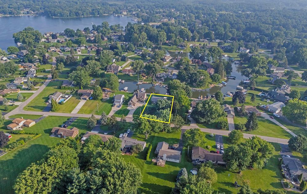 Aerial neighborhood view with highlighted property lot near a lake surrounded by mature trees and homes.