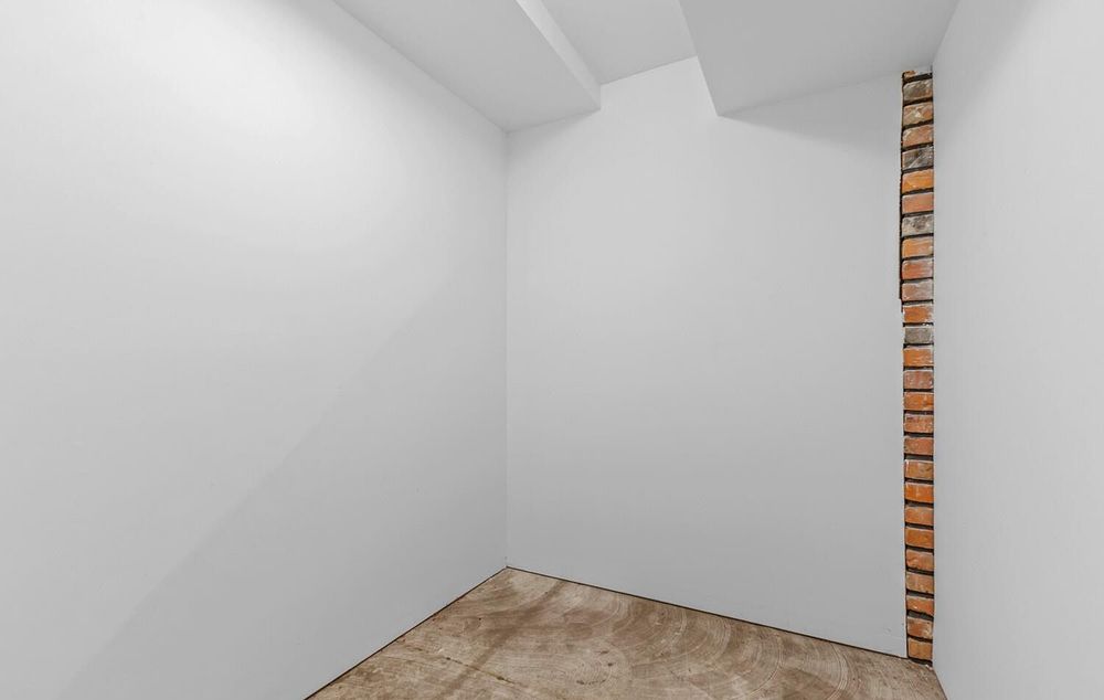 Empty white basement corner room with exposed brick accent column and tile flooring.