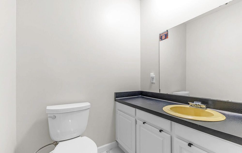 Bathroom with white cabinets, dark countertop, yellow sink bowl, large mirror, and white toilet.