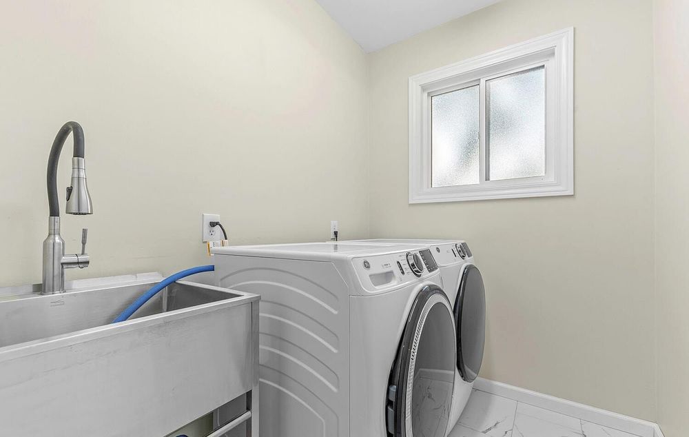 Modern laundry room with front-load washer and dryer, utility sink, and bright window.