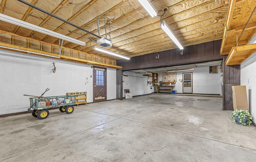 Spacious garage interior with concrete floor, wood ceiling, fluorescent lighting, and storage area.