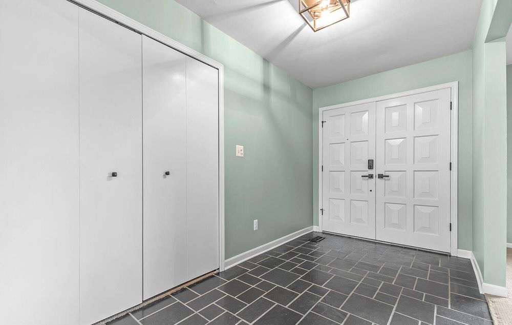 Entryway with slate tile floor, mint green walls, white closet doors, and front door.