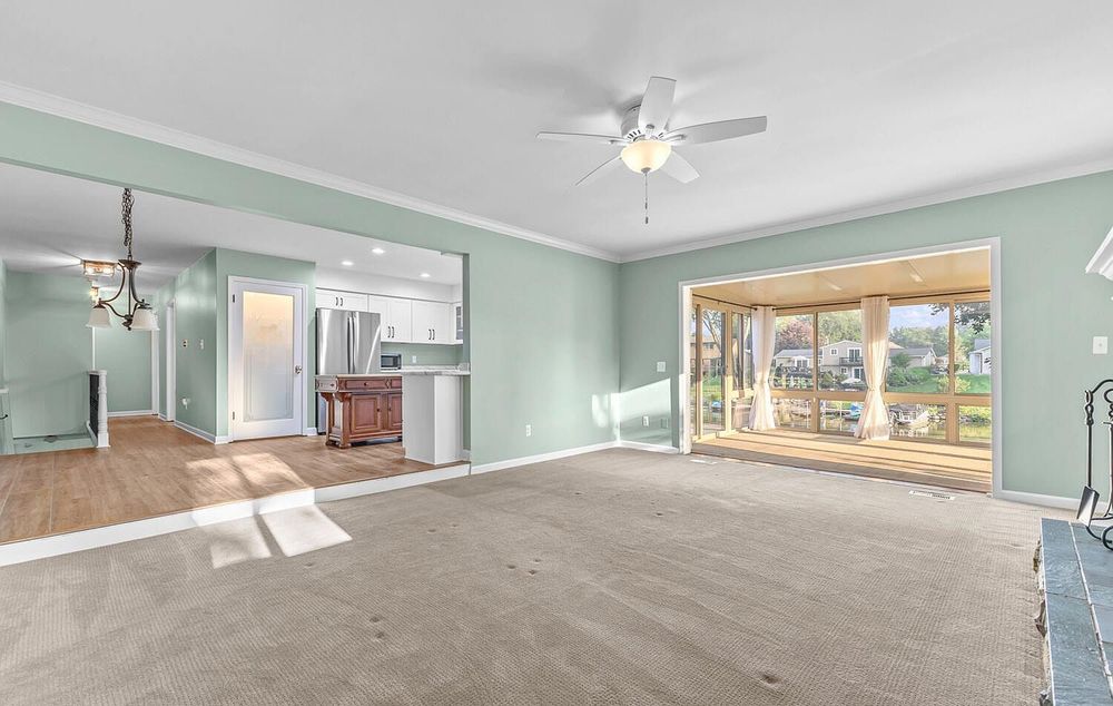 Open living area with carpet, crown molding, ceiling fan, and view into kitchen beyond.