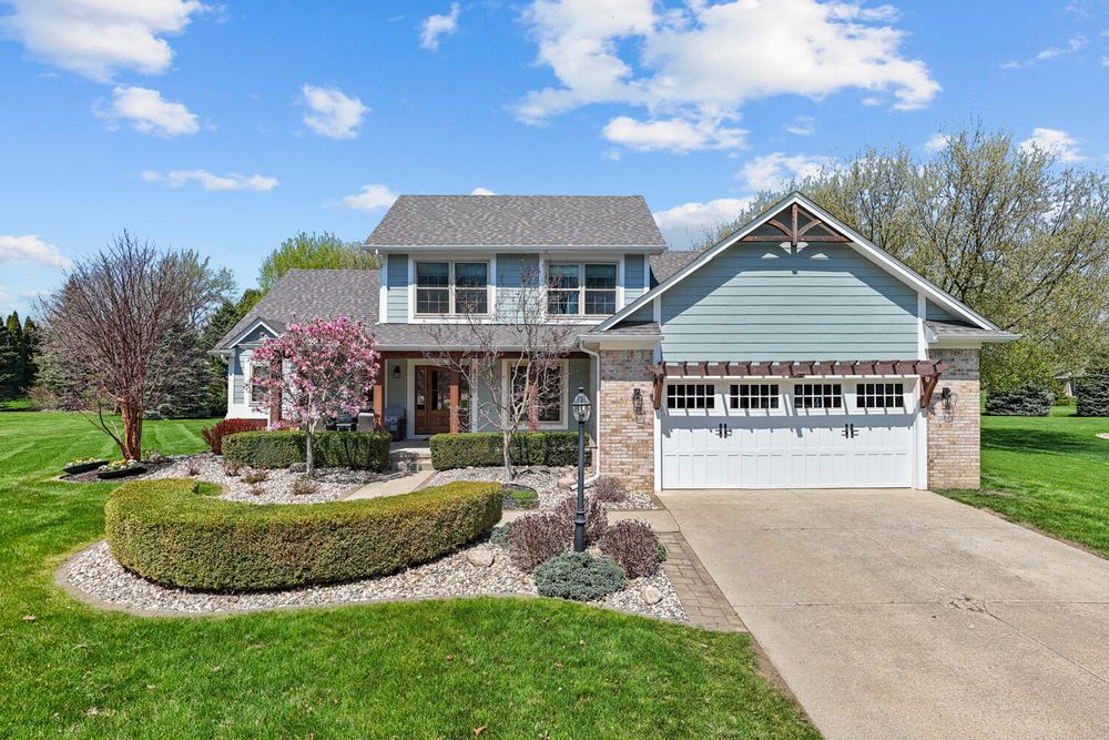 Two-story craftsman home with blue siding, stone accents, two-car garage, and manicured landscaping under a blue sky.