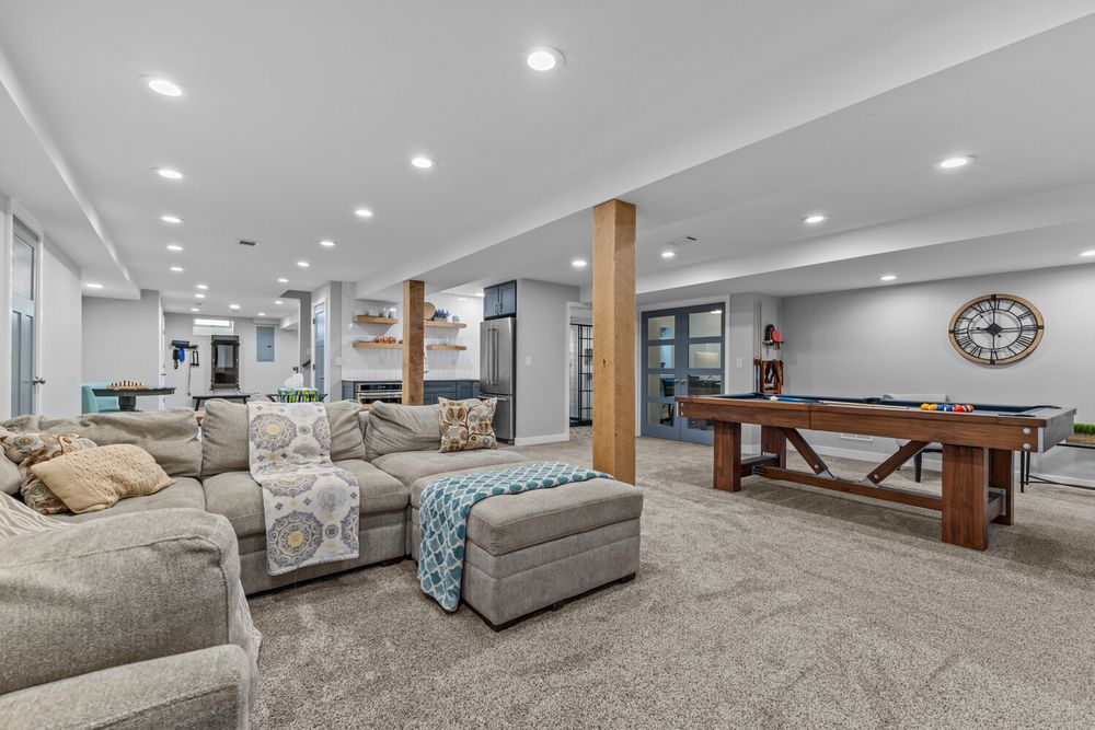 Open-concept finished basement with large sectional sofa, pool table, recessed lighting, and carpeted flooring.