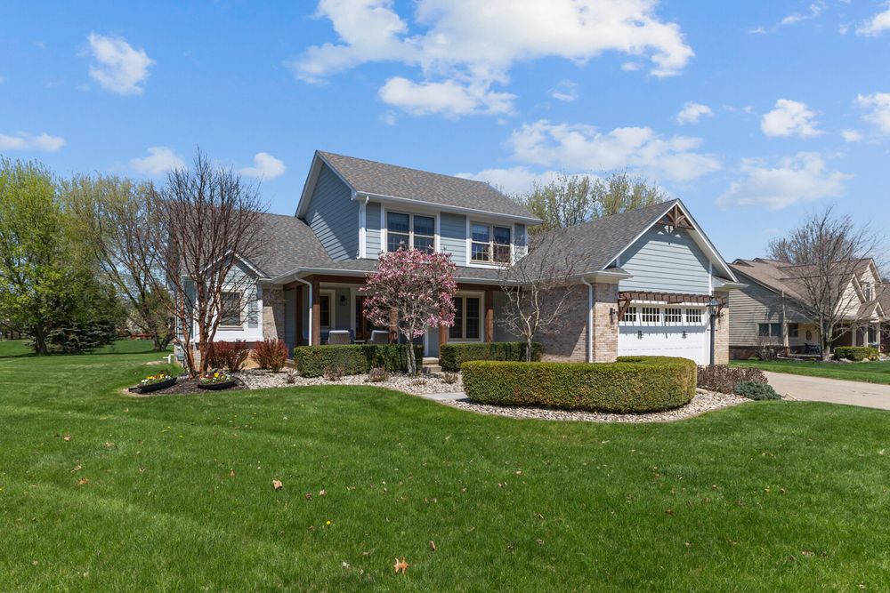 Two-story craftsman home with stone accents, attached garage, manicured landscaping, and blooming trees.