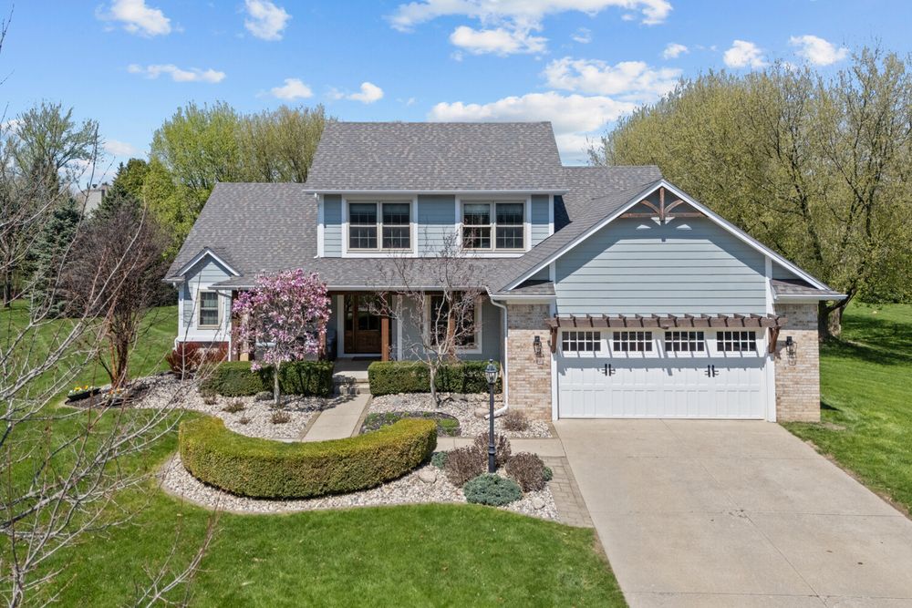 Two-story craftsman home with stone accents, two-car garage, and pink flowering trees in spring.
