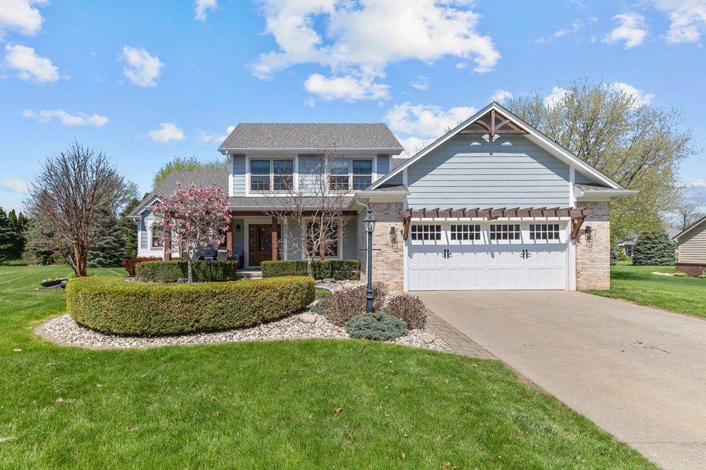 Front exterior of a two-story craftsman-style home with blue siding, stone facade, and circular hedge landscaping.