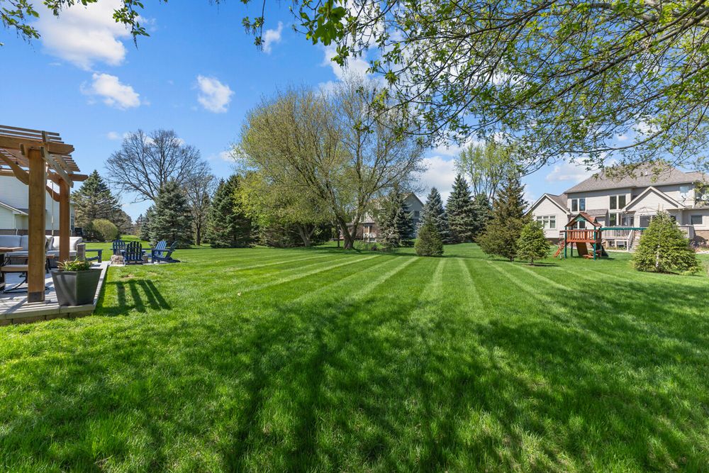 Expansive backyard with striped mowed lawn, mature trees, pergola, and playground equipment on a sunny day.