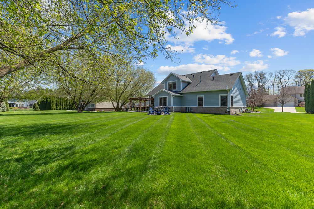 Rear exterior of a craftsman home with blue siding surrounded by a large well-manicured green lawn and trees.