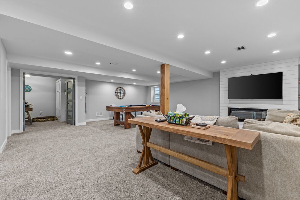 Finished basement with carpeting, recessed lighting, shiplap fireplace, wall-mounted TV, and rustic wood console table.