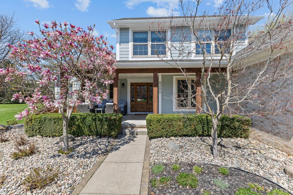 Close-up of craftsman home entrance with blooming magnolia trees, stone pathway, and covered front porch.