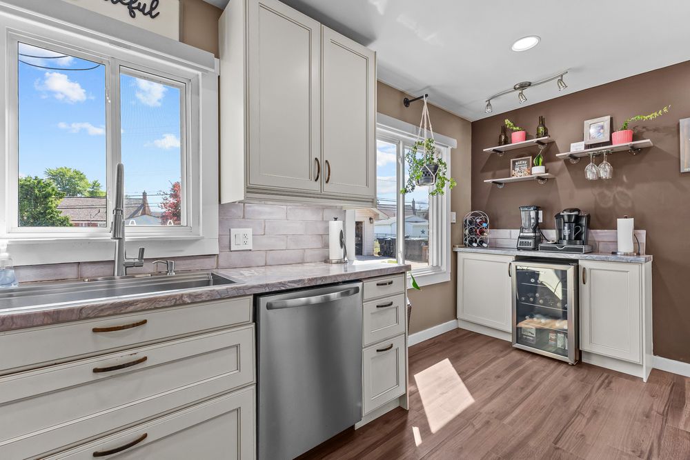 Modern kitchen with white cabinets, subway tile backsplash, stainless steel dishwasher, and wine cooler.