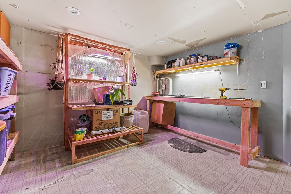 Unfinished basement workshop area with wooden workbench, shelving, and pink painted concrete floor.