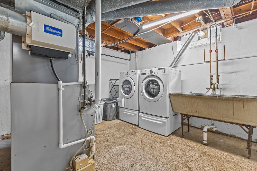 Basement laundry room with washer, dryer, utility sink, and exposed ceiling ductwork.