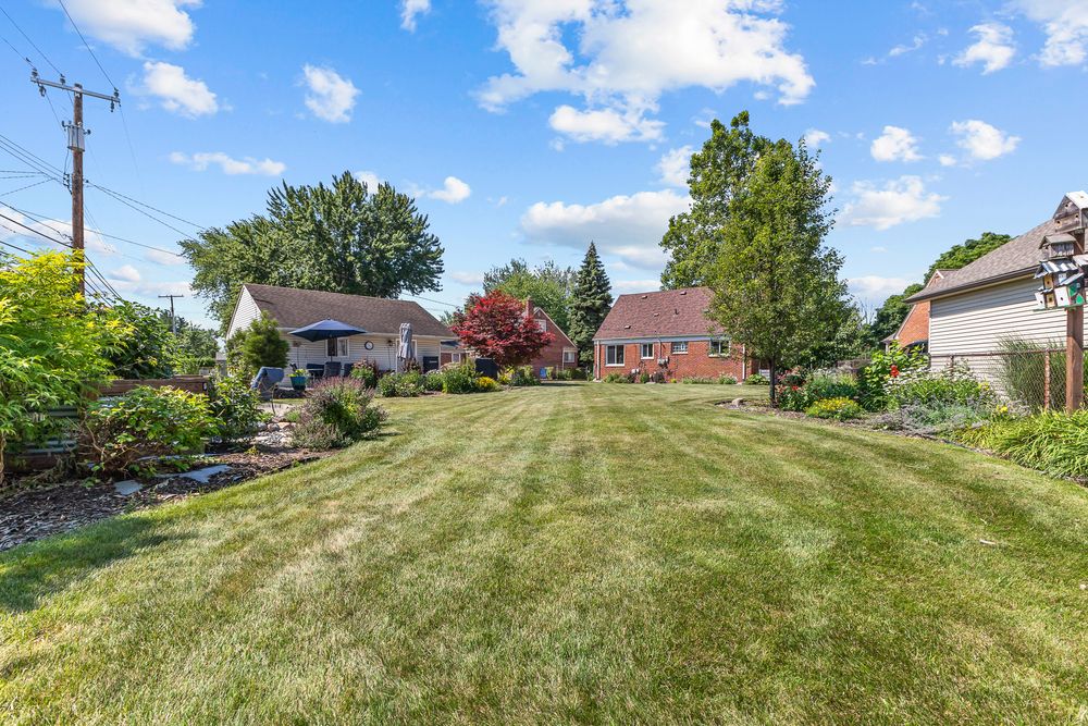 Spacious backyard with well-manicured lawn, mature trees, and brick home exterior.