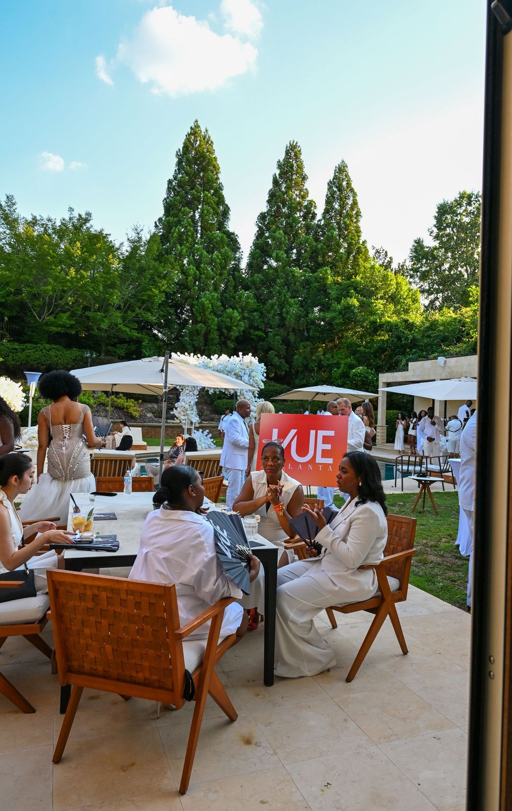 Guests in white attire socializing at an outdoor garden party with a VUE branded banner.