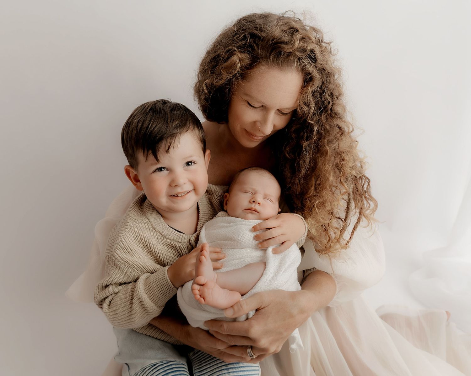 Mother holding newborn baby and toddler during newborn studio session