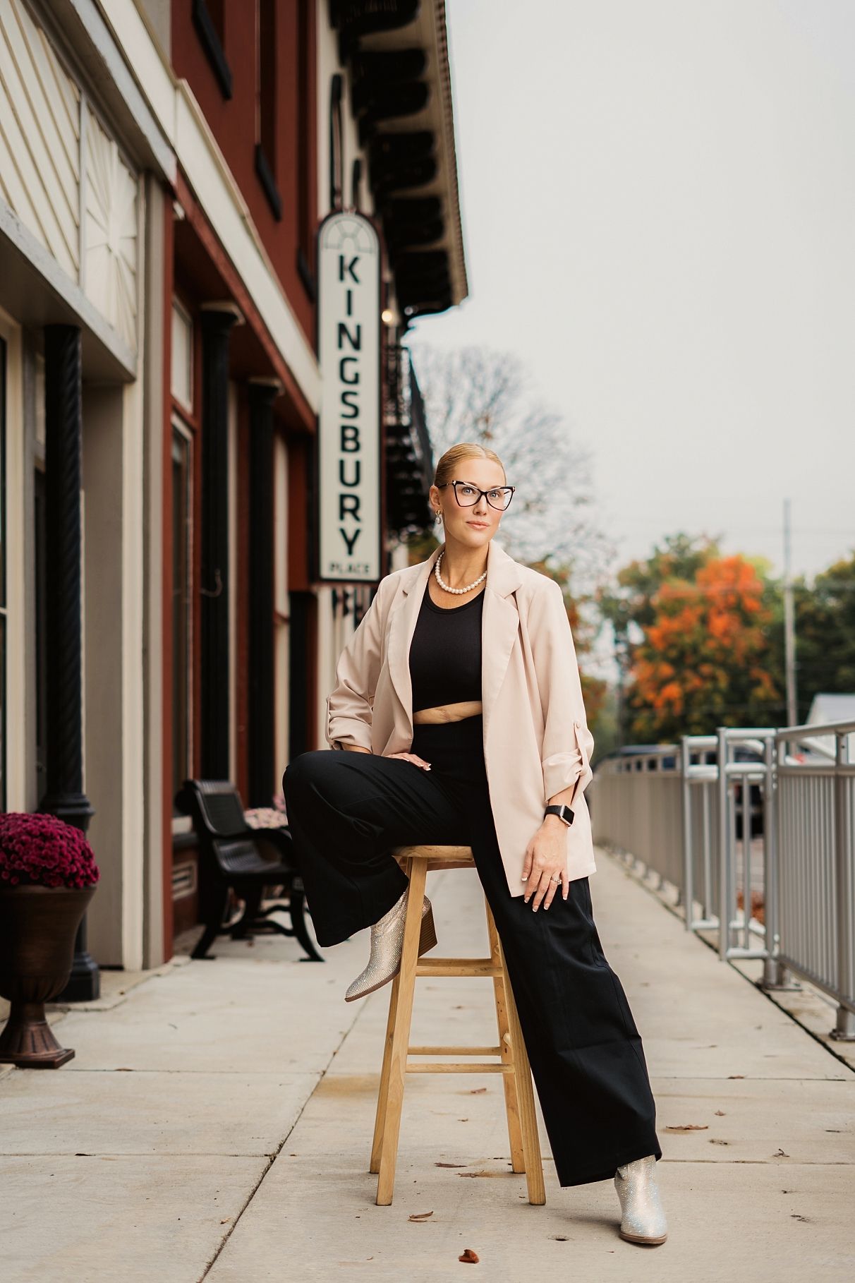 Stylish woman in black outfit and pink blazer poses on stool outside Kingsbury Place.