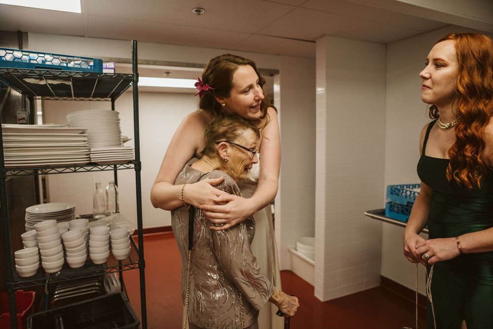 Two women sharing a warm hug in a catering area while a third woman in a green dress looks on.
