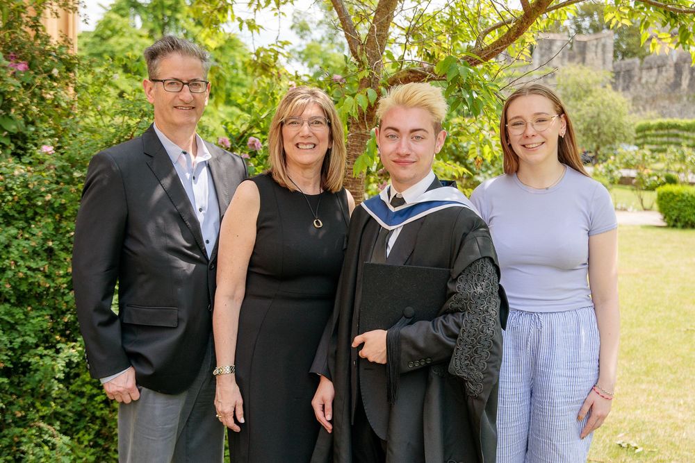 Group graduation photos taken in a sunny garden setting with traditional architecture.