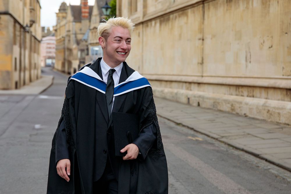 Graduate walking along historic stone buildings and pathways in academic regalia.