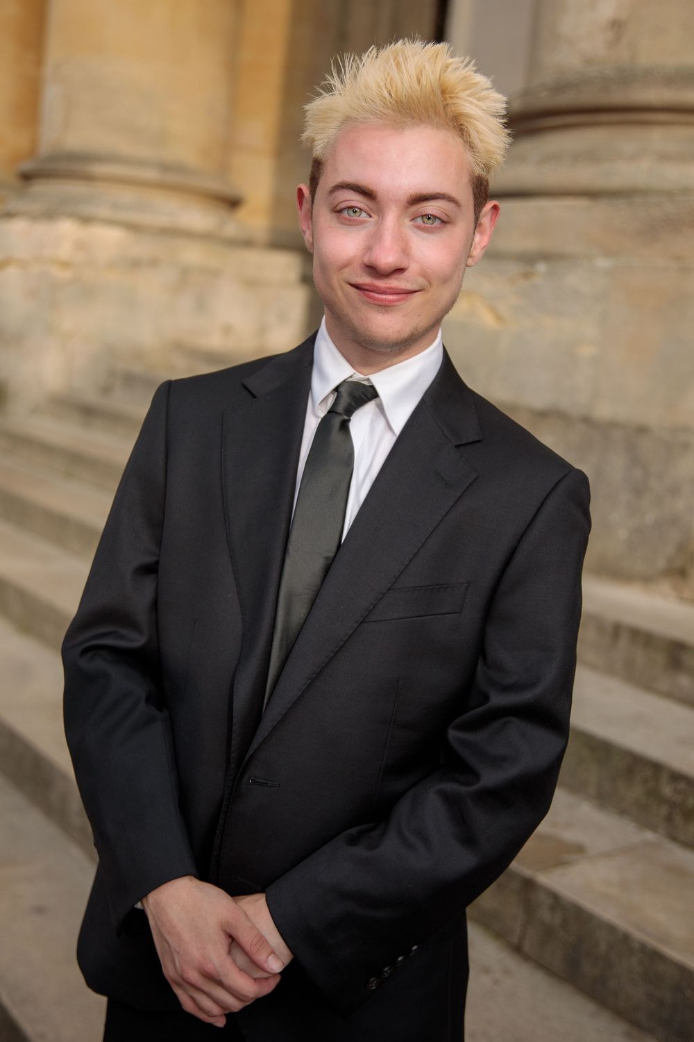Professional headshots of a person in a black suit against a stone architectural background.
