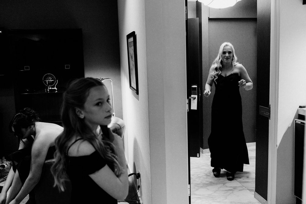 Black and white photo of two women in elegant black gowns, one posing in a doorway mirror reflection at a formal event.