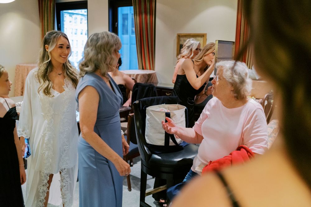 Bride in white gown laughing with guests during wedding preparations in historic Chicago hotel suite.