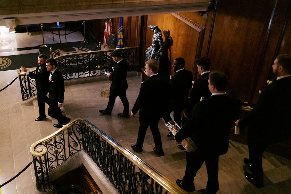 Wedding party in black tuxedos descending The Union League Club of Chicago's grand staircase in elegant venue before formal ceremony.