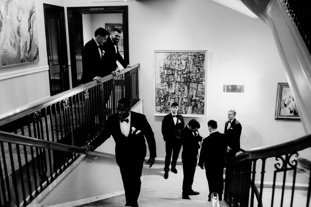 35mm film photo of groomsmen in tuxedos gather on a grand staircase in a historic Chicago hotel adorned with fine art paintings.