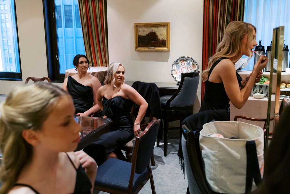 Bridesmaids in black dresses relax and apply makeup in a bridal suite before wedding.