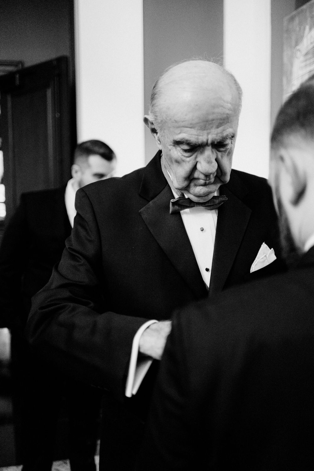Elderly man in tuxedo with bow tie shares emotional moment, captured in black and white photography.