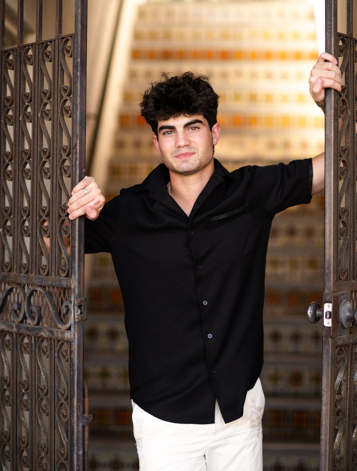Young man in black shirt posing between ornate iron gates.
