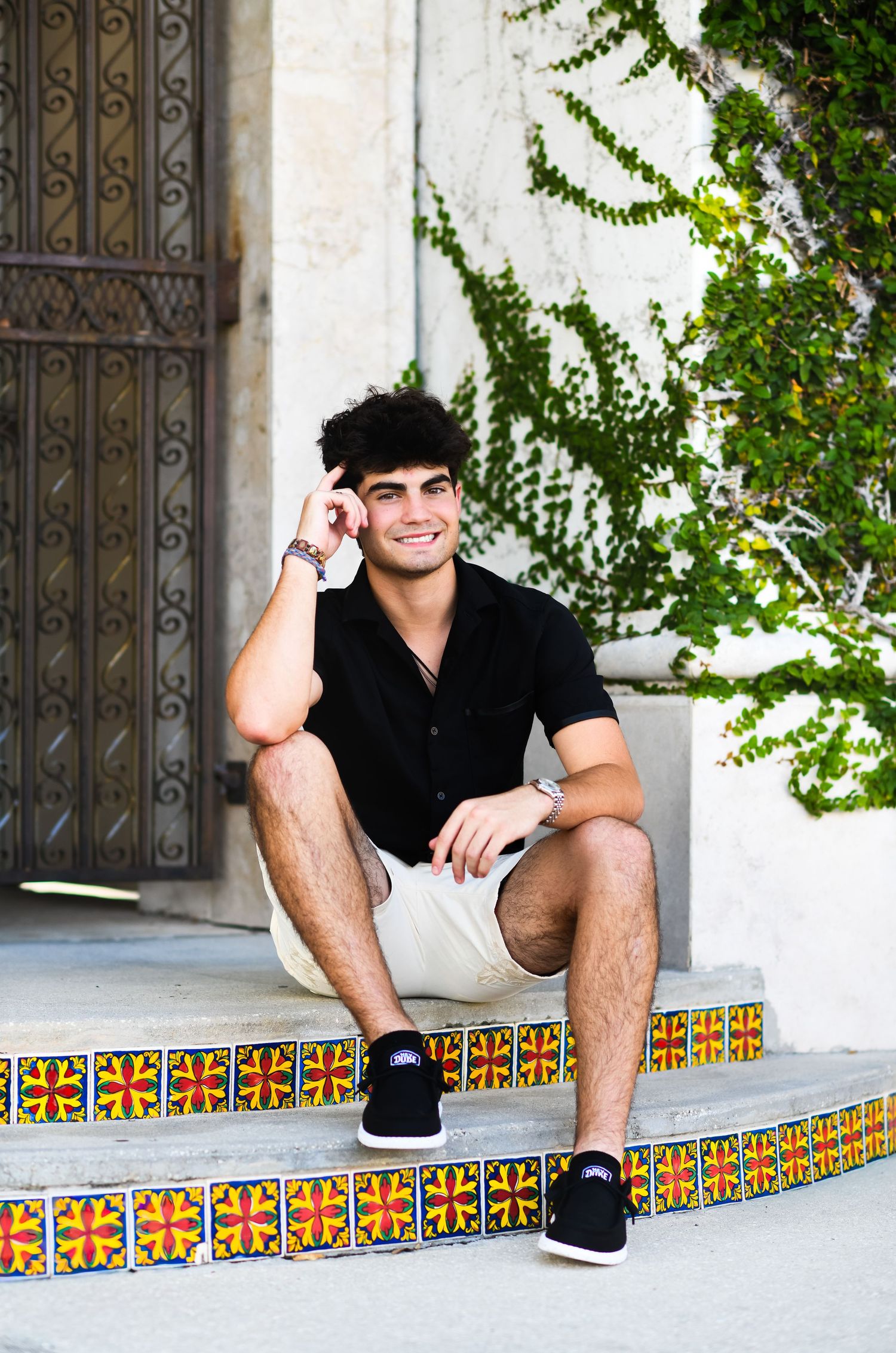 Smiling young man in black shirt sitting on colorful tiled steps outdoors.
