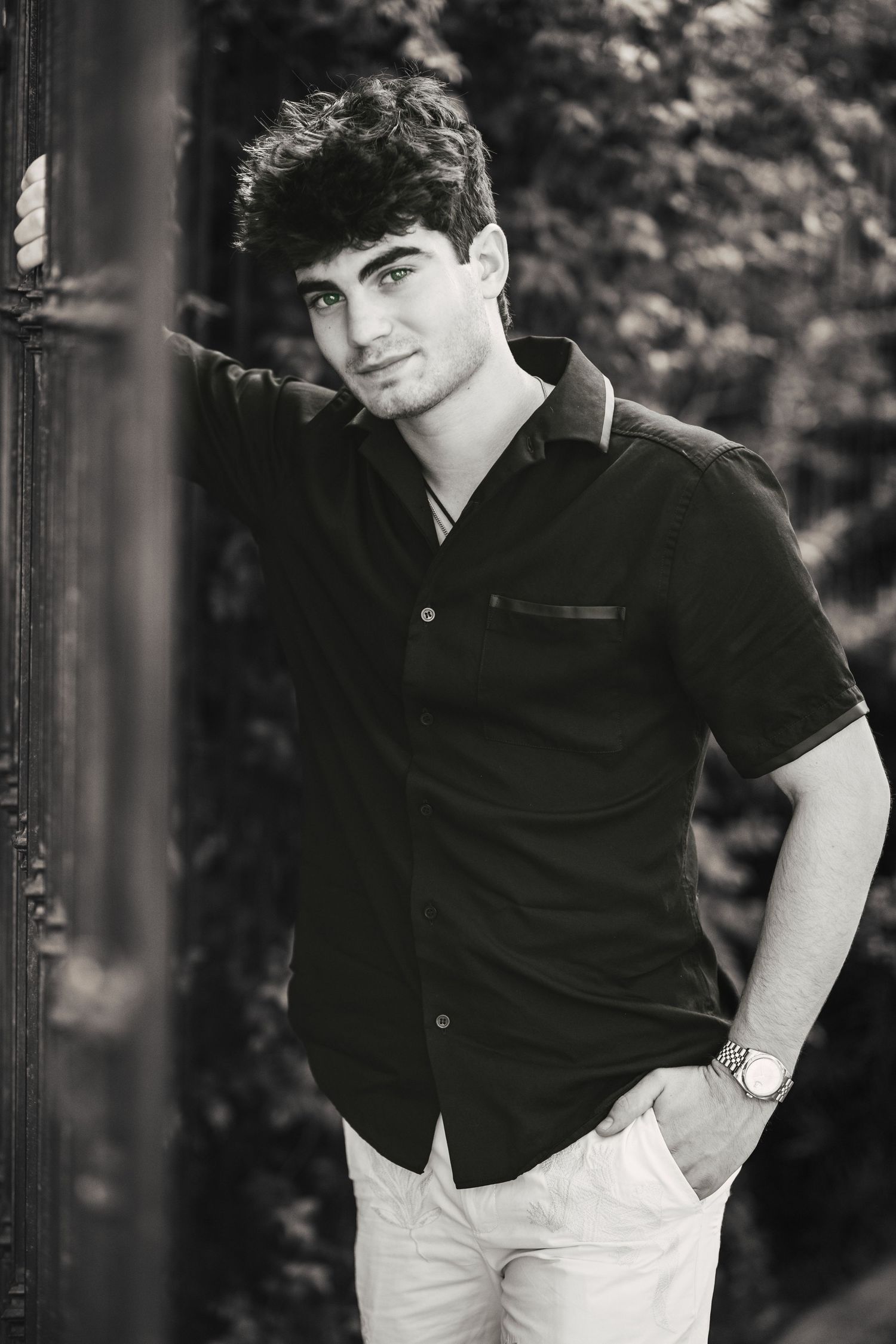 Stylish young man in black shirt leaning against post in black and white portrait photo.