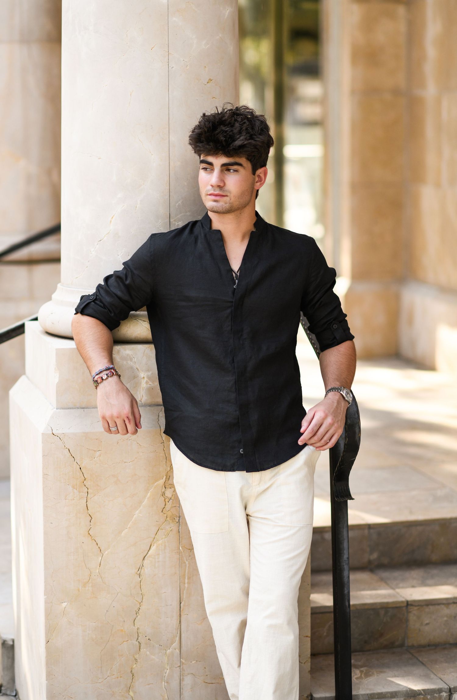 Handsome young man in black shirt leaning against marble column on outdoor steps.