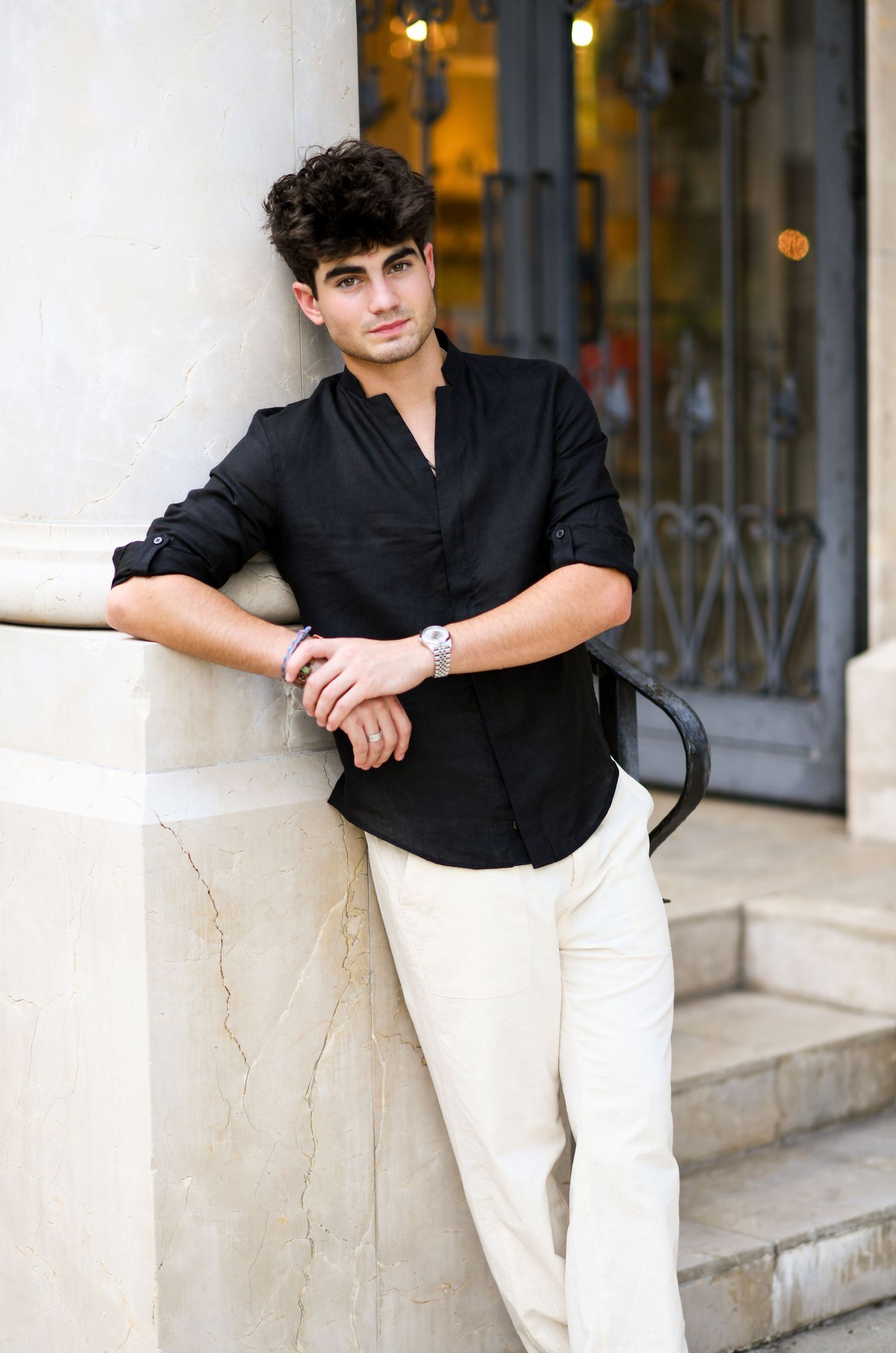 Young man in black long-sleeve shirt leaning against marble column on steps.