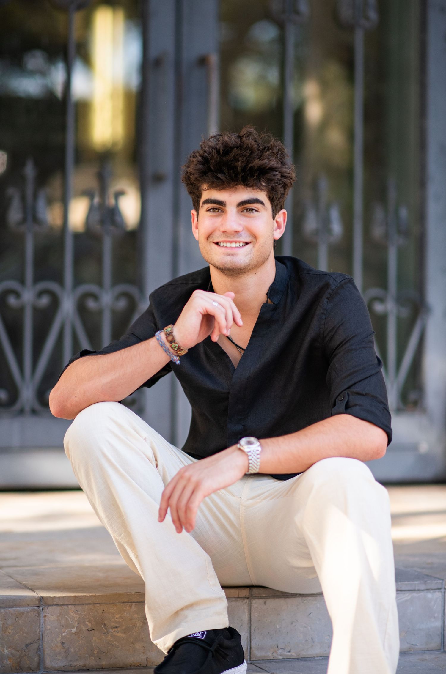Smiling young man in black shirt sitting on steps outdoors in warm sunlight.