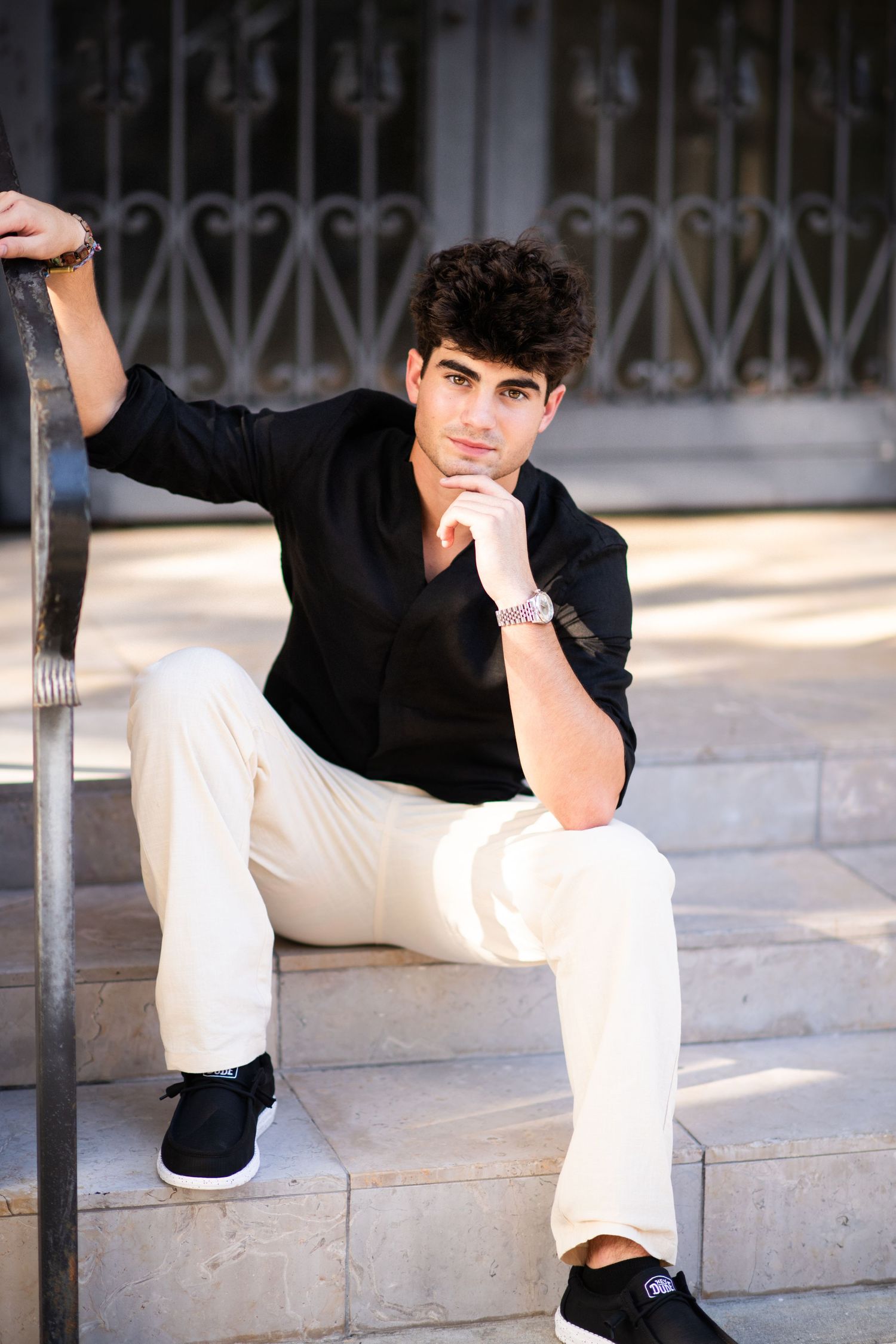 Young man in black shirt and cream pants sitting on stone steps in contemplative pose.