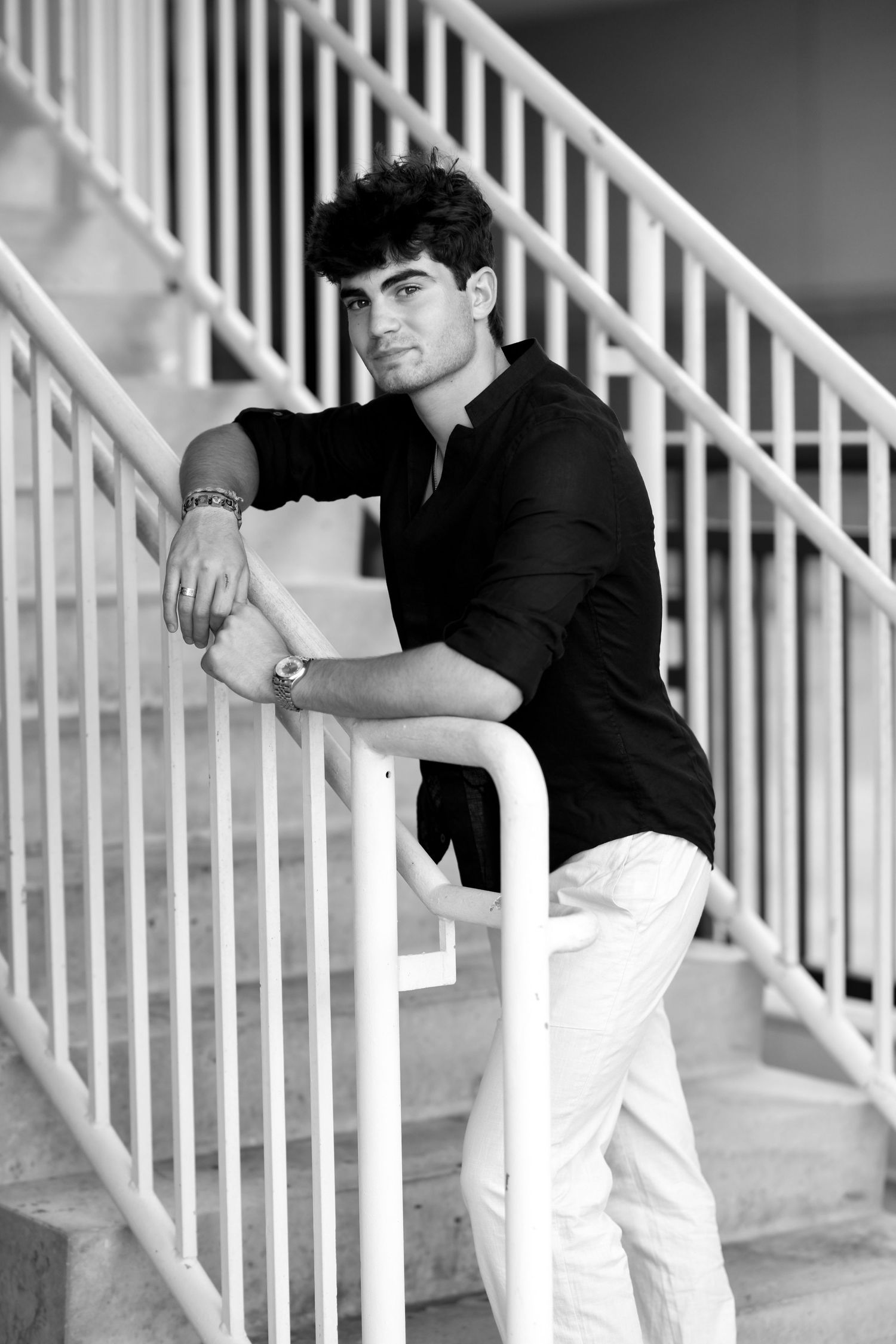 Stylish young man in black shirt leaning on white stair railing in black and white photo.