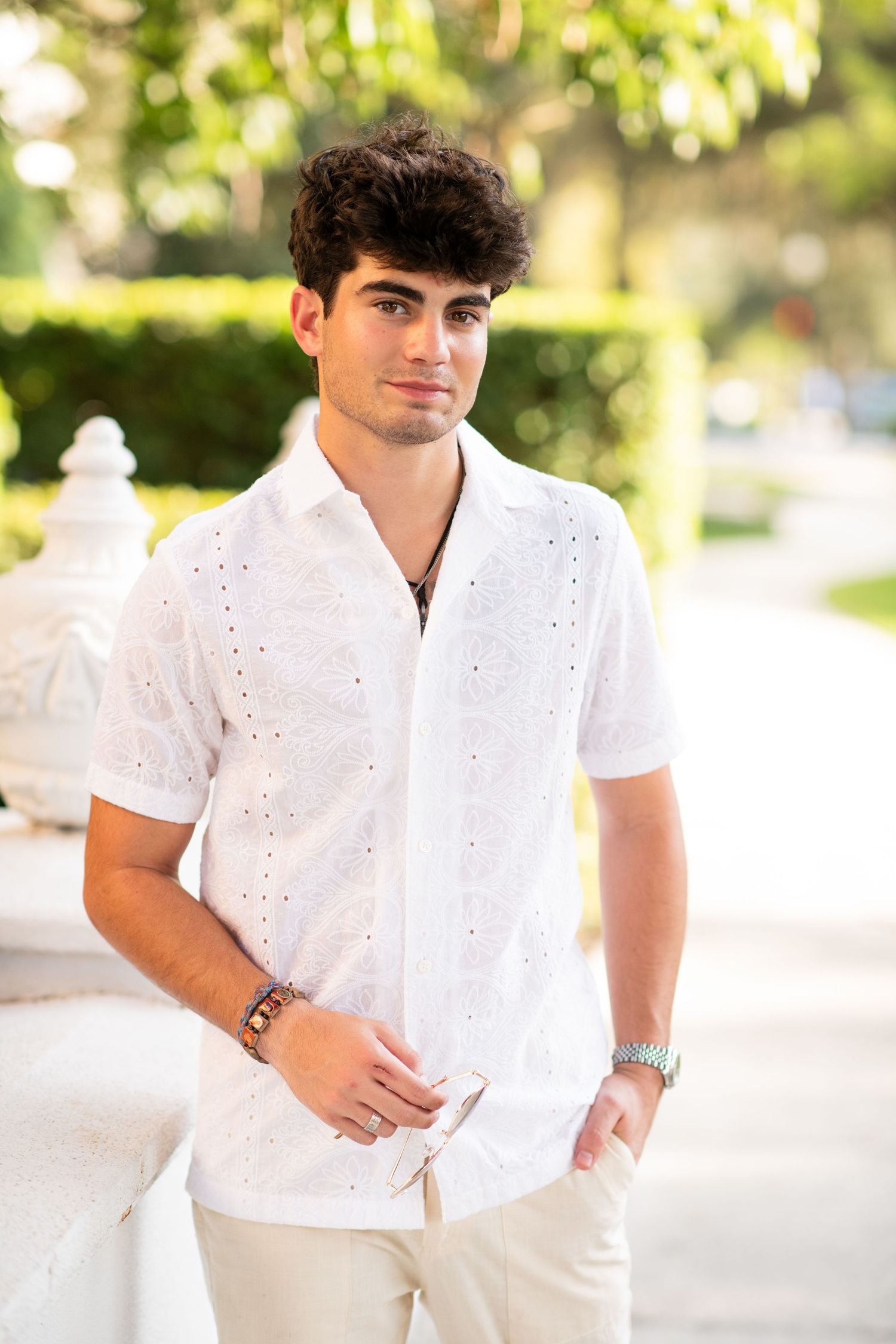 Young man in white eyelet short-sleeve shirt standing in sunny outdoor setting.