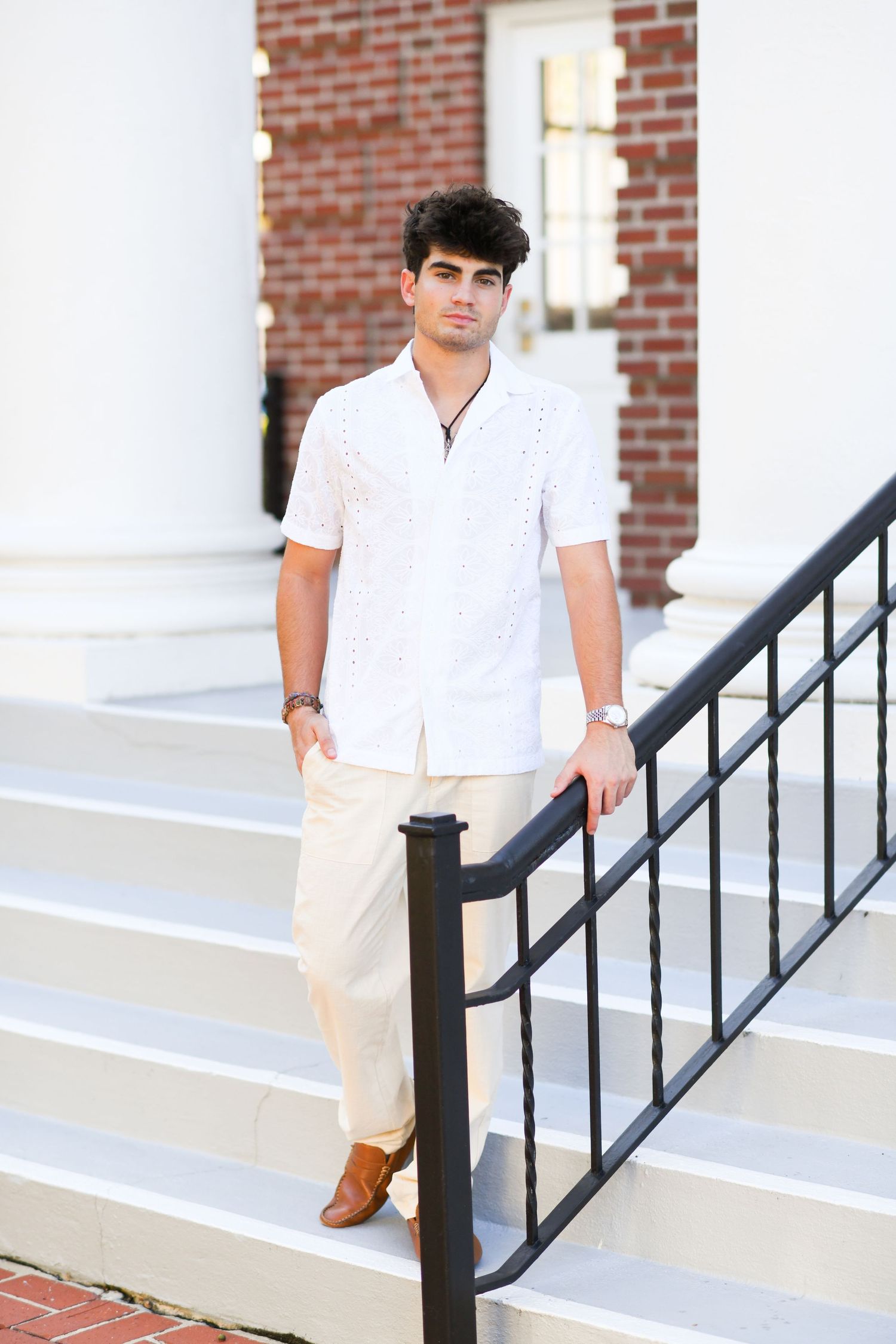 Young man in white short-sleeve shirt on white steps with black railing.