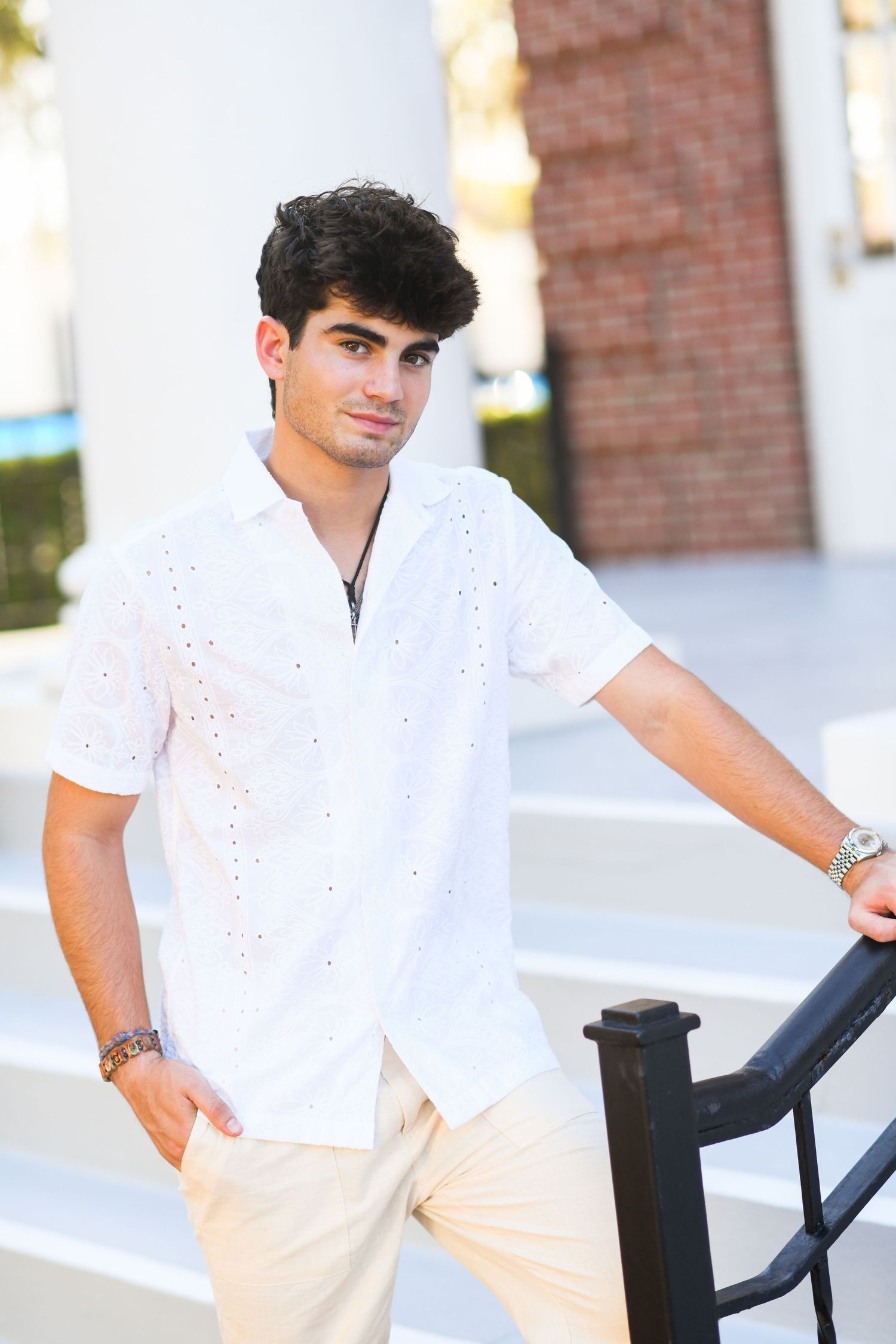 Young man in white eyelet short-sleeve shirt leaning on a black railing.