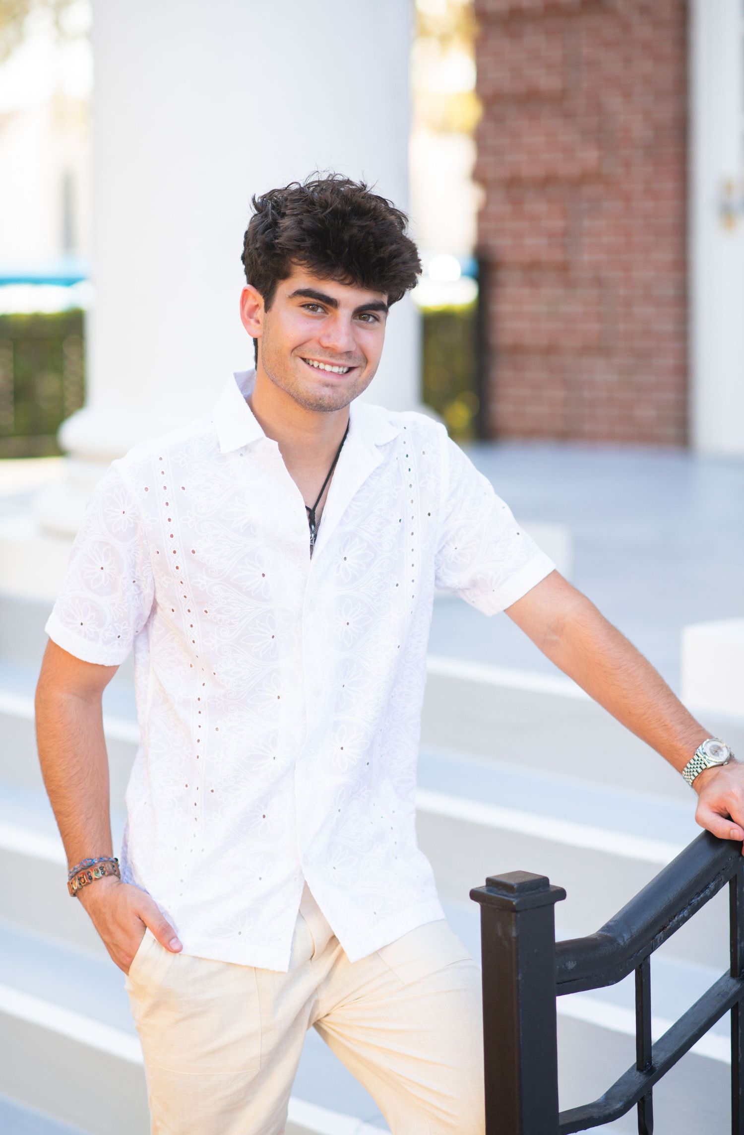 Smiling young man in white shirt leaning on railing outdoors.