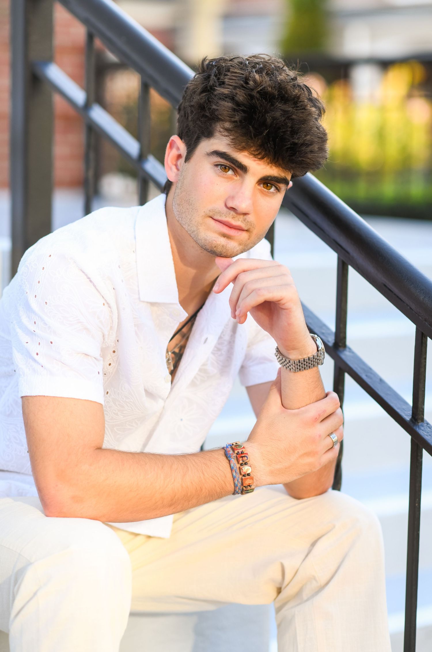 Young man in white eyelet shirt sitting on steps with hands clasped in thoughtful pose.