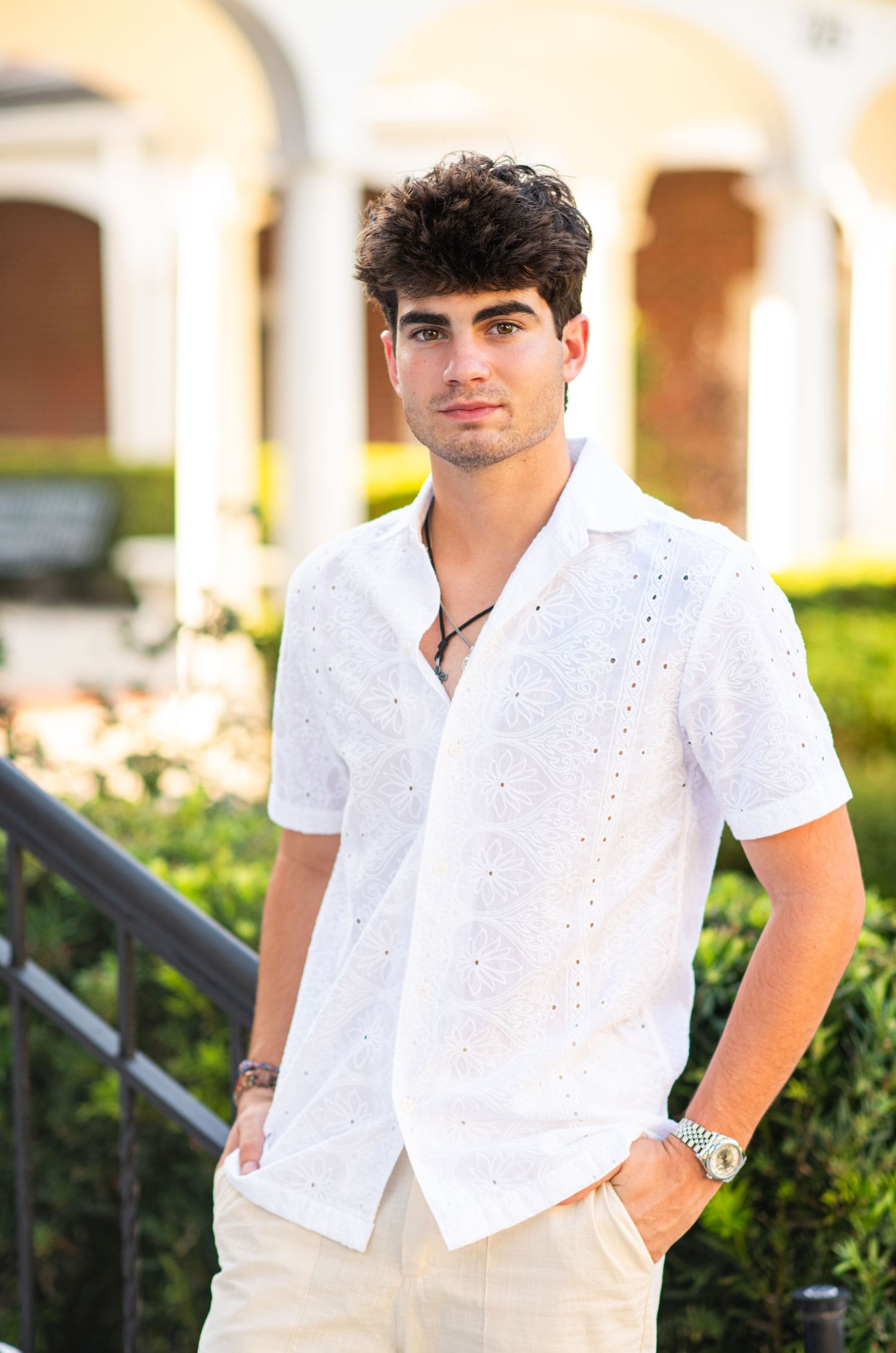 Young man in white eyelet short-sleeve shirt posing outdoors with columns in background.
