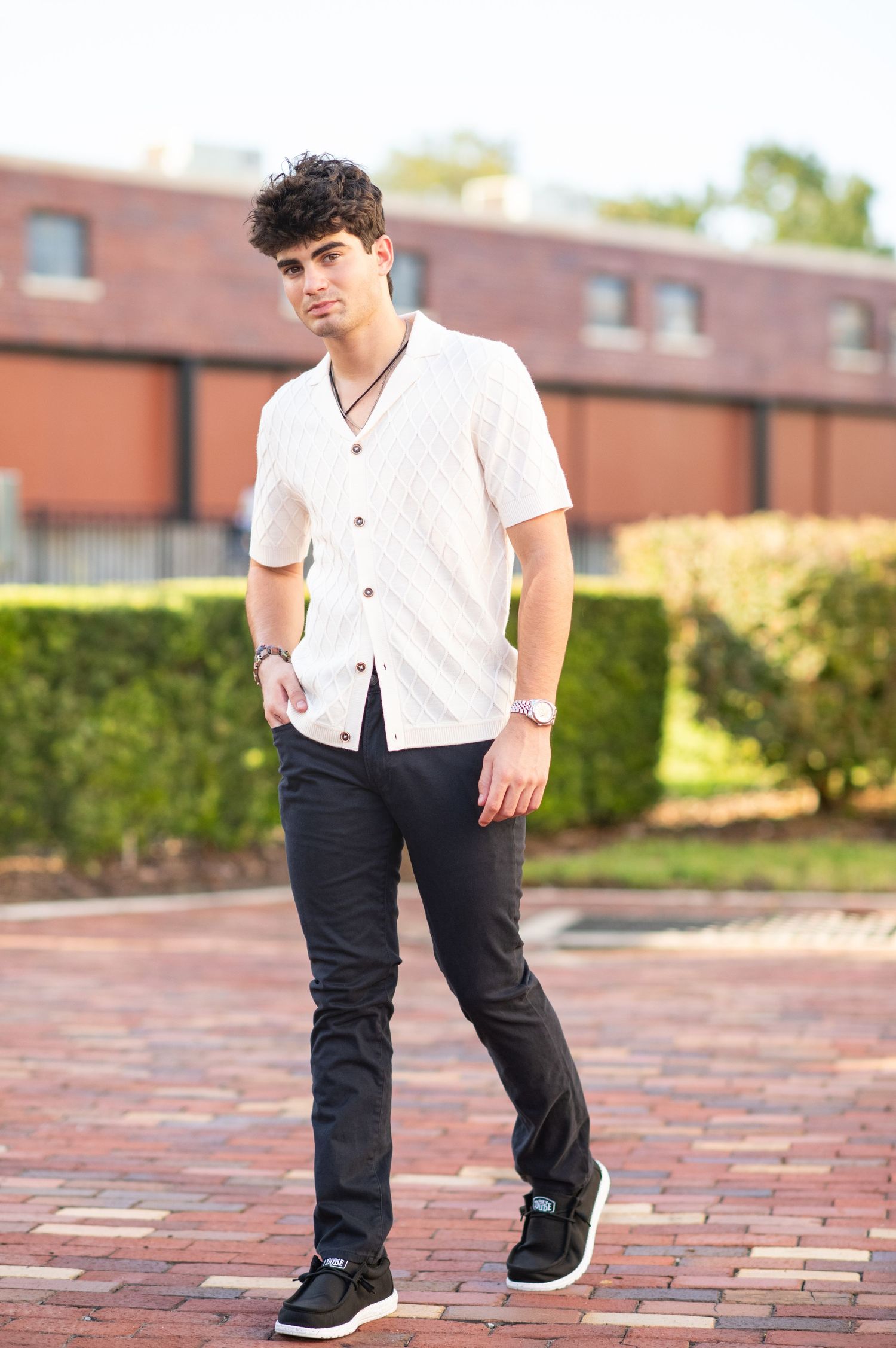 Young man in white button-up shirt and black pants posing on brick plaza outdoors.