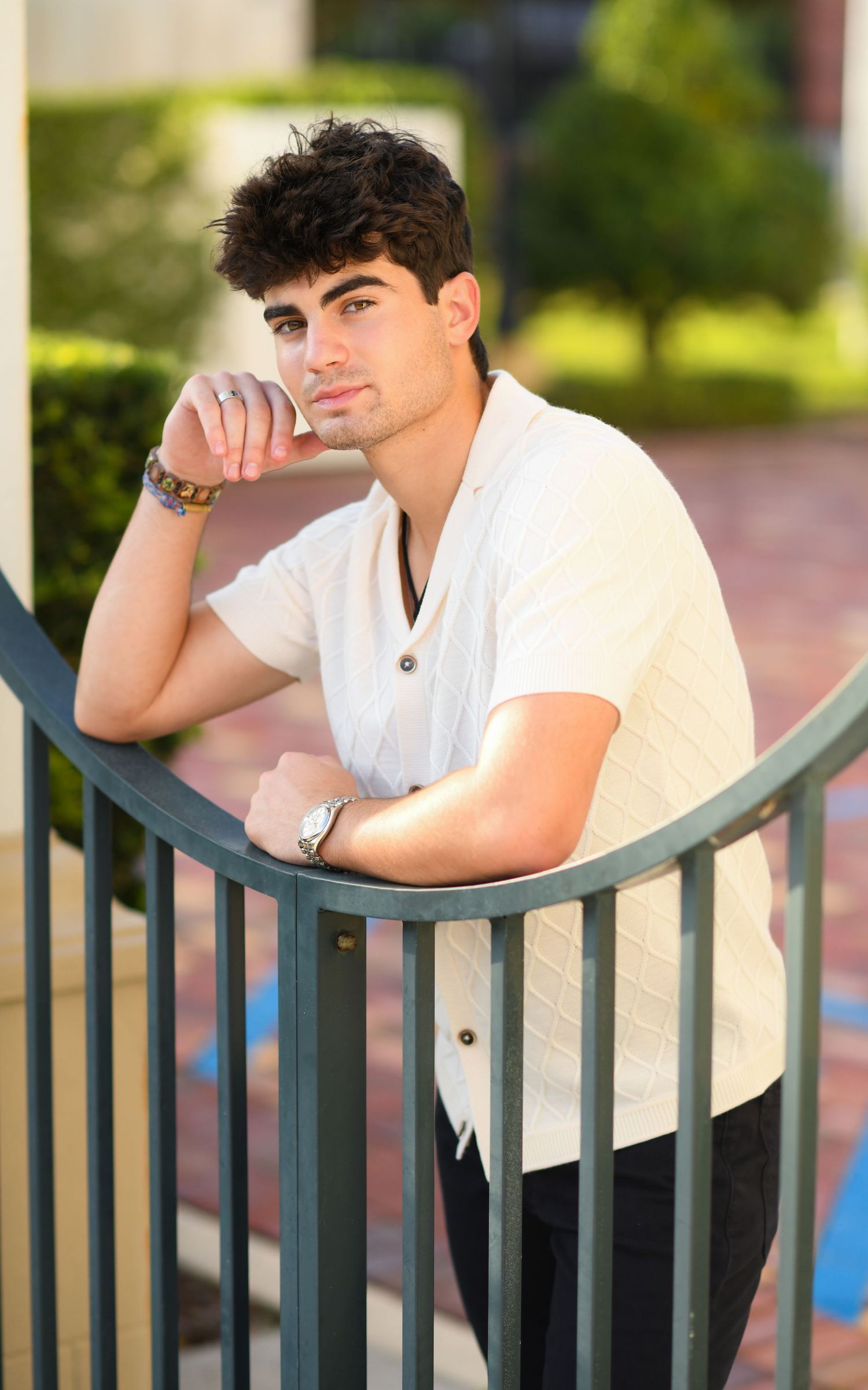 Young man in cream knit shirt leaning thoughtfully on a metal railing.