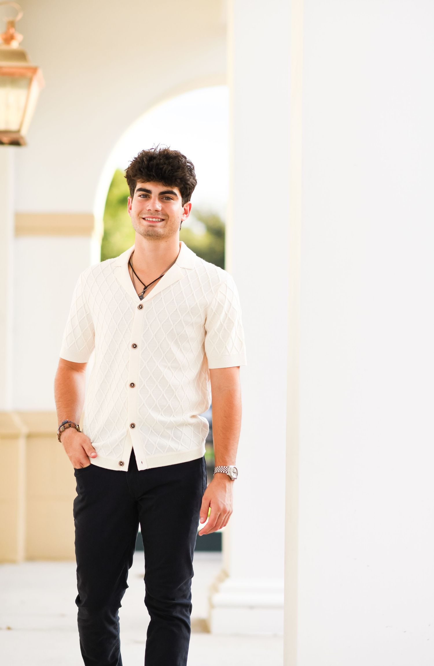 Smiling young man in cream patterned shirt walking through white archway.